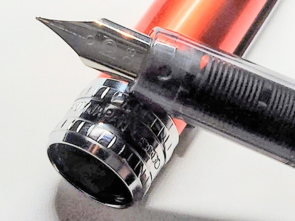 外したキャップの上にペン先を置いたプラチナ万年筆プレジール。ノバオレンジの質感と造形が際立つ拡大写真