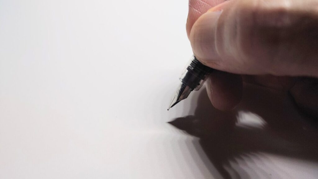 万年筆を正しく持つ指の位置とペン先の向きがわかる画像。親指・人差し指・中指で三角形を作り、ペン先の刻印が上を向くように持つ基本フォームを示している。