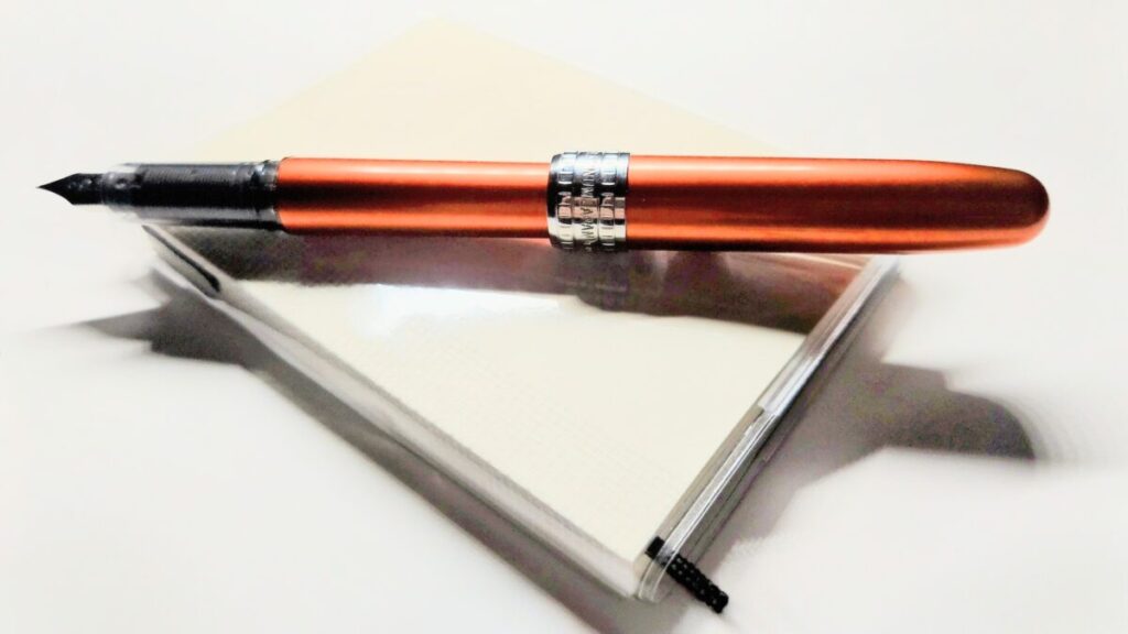 メモ帳の上にキャップポストされたプラチナ万年筆プレジール。使用前の状態で静かに置かれている