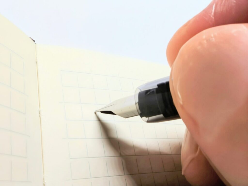 プラチナ万年筆プレジールのペン先がメモ帳に触れた瞬間。軽い筆圧で書き始めるシーン