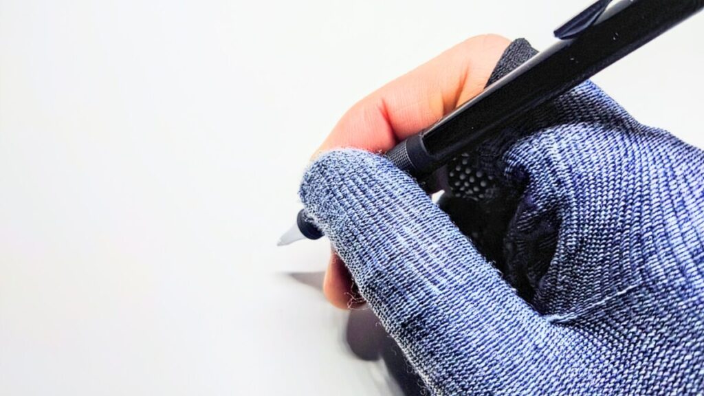 青い手袋をした手が白い机の上でオレンズ メタルグリップを握っている様子。金属グリップの質感とフィット感が伝わる。